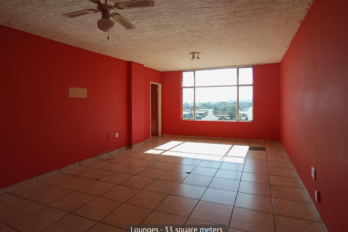 Spacious, empty living area featuring tiled flooring, a ceiling fan, and large windows providing natural light and exterior views.