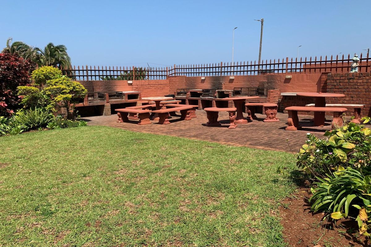 A spacious outdoor rear garden area featuring a paved patio with built-in brick braai facilities and perimeter fencing.