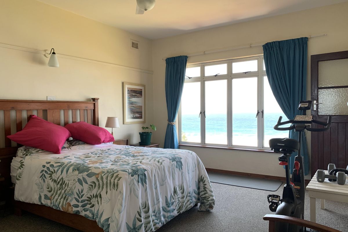 A spacious bedroom featuring a large window with ocean views, neutral wall tones, carpeted flooring, and a ceiling fan.