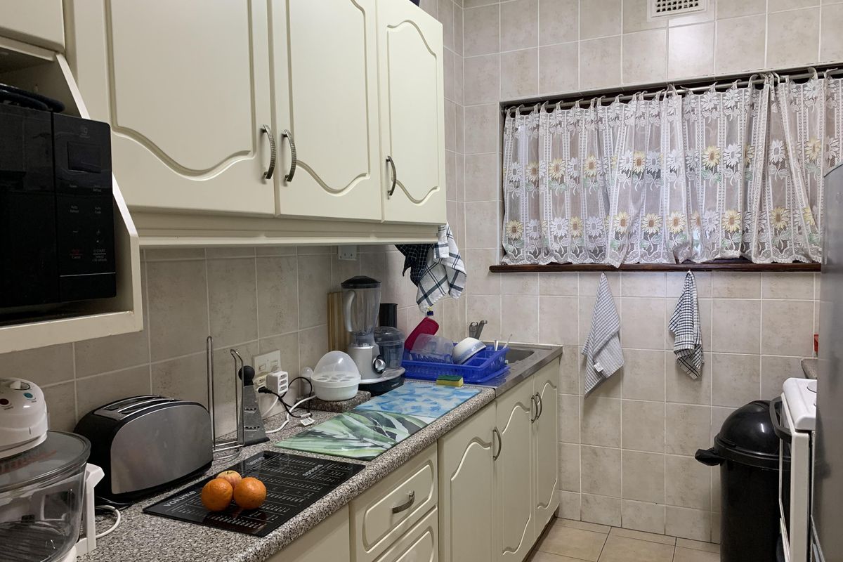 A functional kitchen featuring traditional cream cabinetry, tiled walls, and durable laminate countertops with a stainless steel sink.
