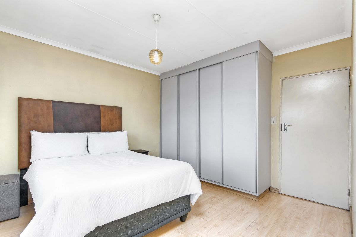 A bedroom featuring light laminate flooring, a large grey built-in wardrobe, and neutral wall tones, providing a functional and well-lit sleeping space.