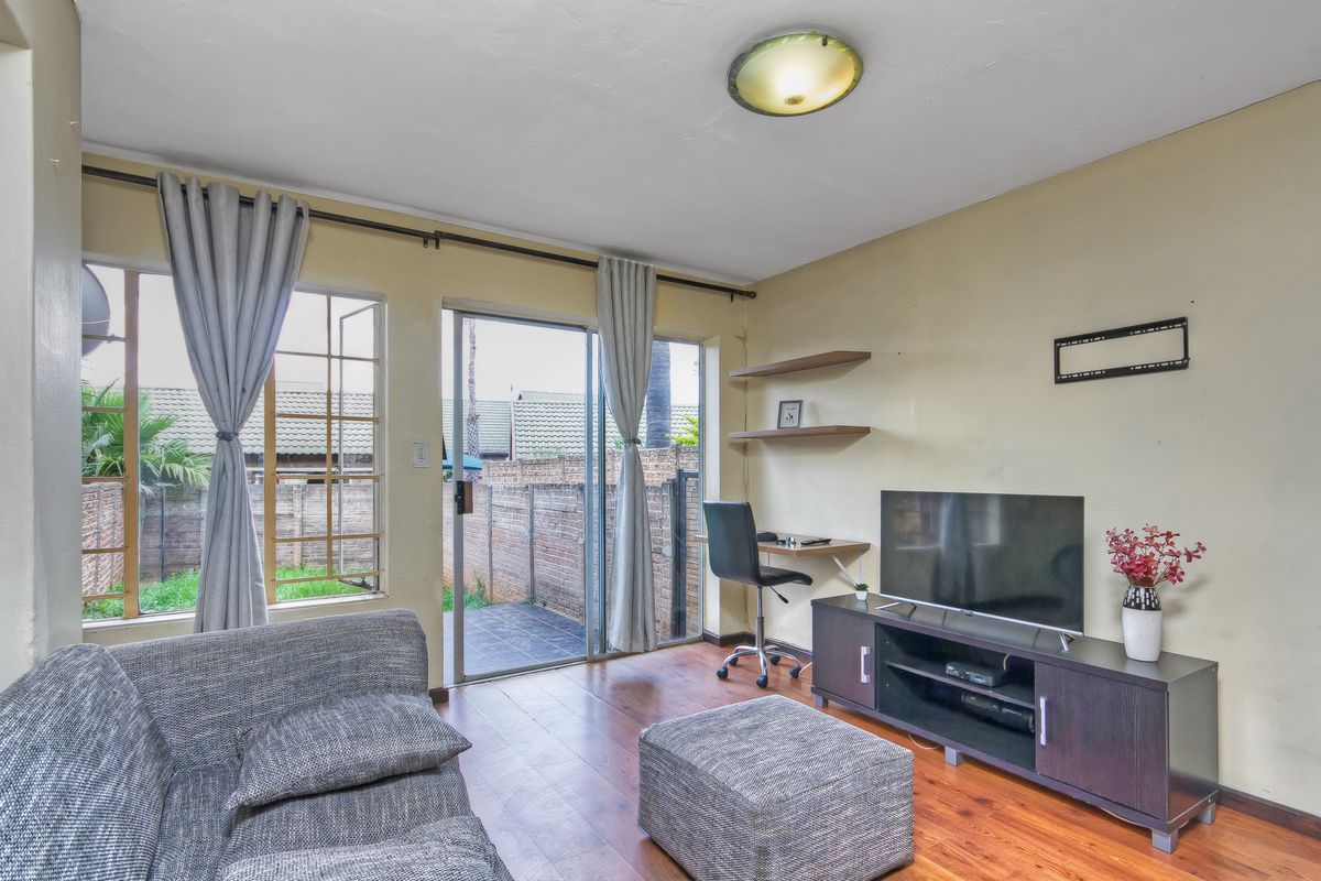 A living room featuring wooden flooring, floating shelves, and a sliding glass door providing access to the outdoor area.