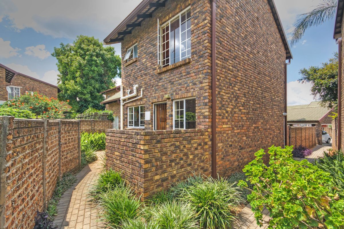 A view of the rear exterior of the face brick apartment building, featuring a paved walkway and established garden borders.