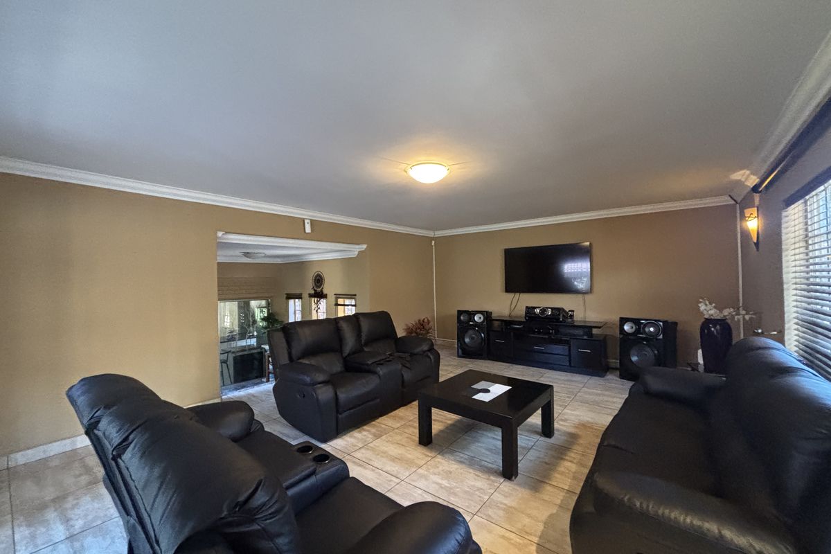 Spacious living room featuring tiled flooring, crown molding, and a wall-mounted television, offering a comfortable and functional layout for relaxation.