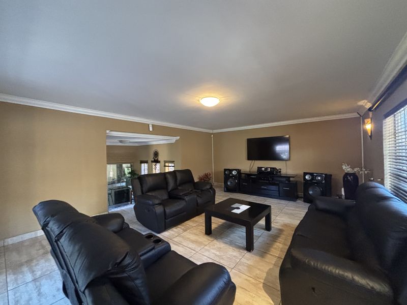 Spacious living room featuring tiled flooring, crown molding, and a wall-mounted television, offering a comfortable and functional layout for relaxation.