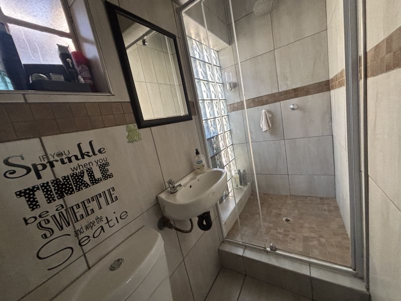 Compact bathroom featuring a shower enclosure, wall-mounted basin, toilet, and decorative glass block window with neutral wall tiling.