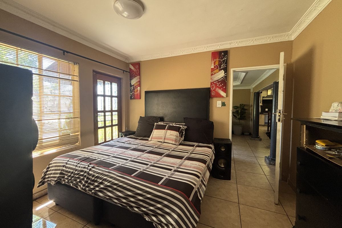 A bedroom featuring tiled flooring, crown molding, and a french door leading to the exterior, with natural light filtered through venetian blinds.