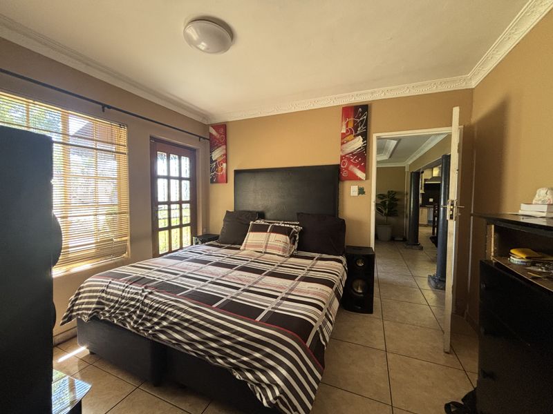 A bedroom featuring tiled flooring, crown molding, and a french door leading to the exterior, with natural light filtered through venetian blinds.