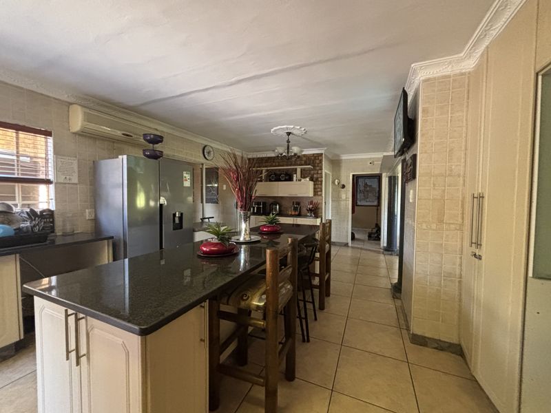 Spacious kitchen featuring a large granite-topped island, tiled flooring, built-in cabinetry, and an exposed brick feature wall, offering a functional layout for cooking and dining.