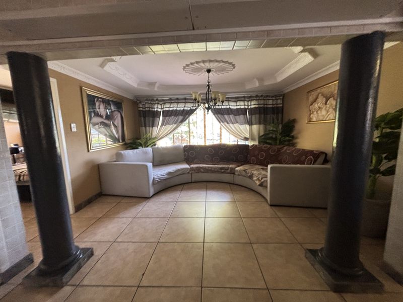 A living room featuring ceramic floor tiles, decorative ceiling cornices, a central ceiling rose, and structural columns framing the space.