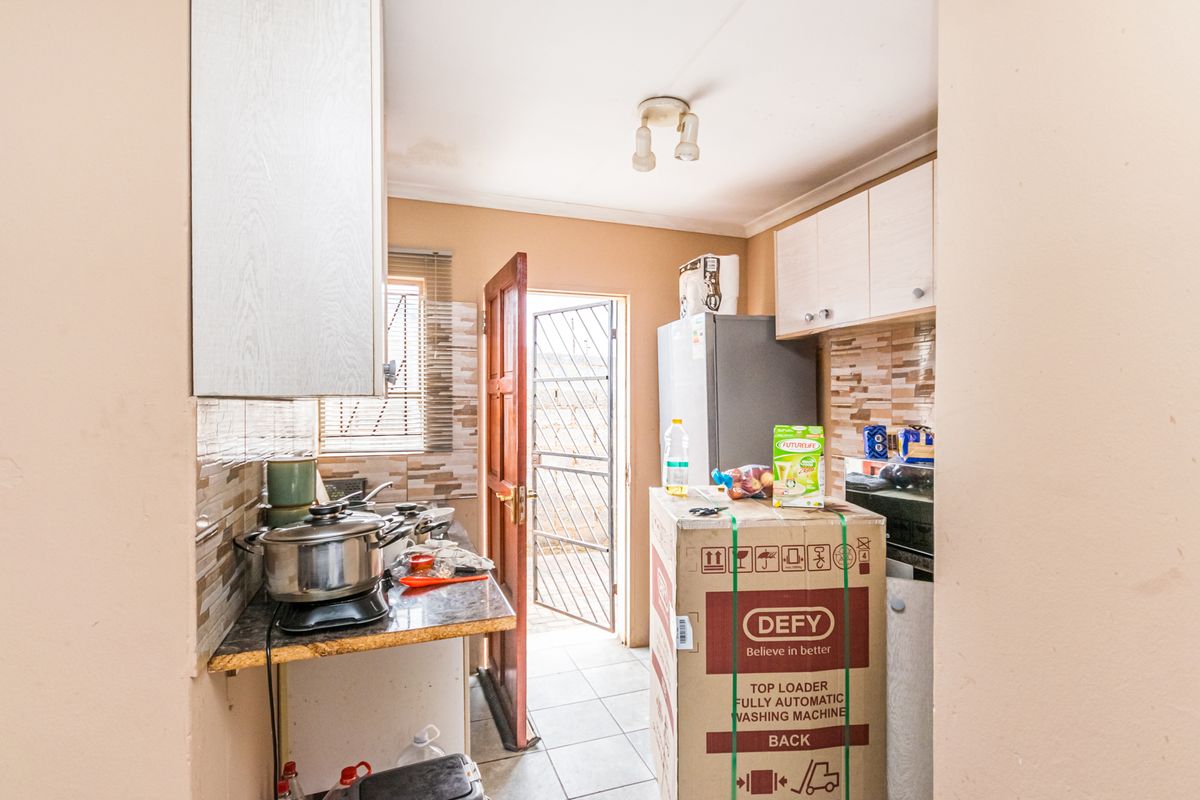 Compact kitchen featuring tiled backsplash, built-in cabinetry, and direct access to an exterior security gate.