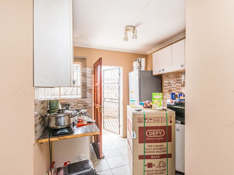 Compact kitchen featuring tiled backsplash, built-in cabinetry, and direct access to an exterior security gate.