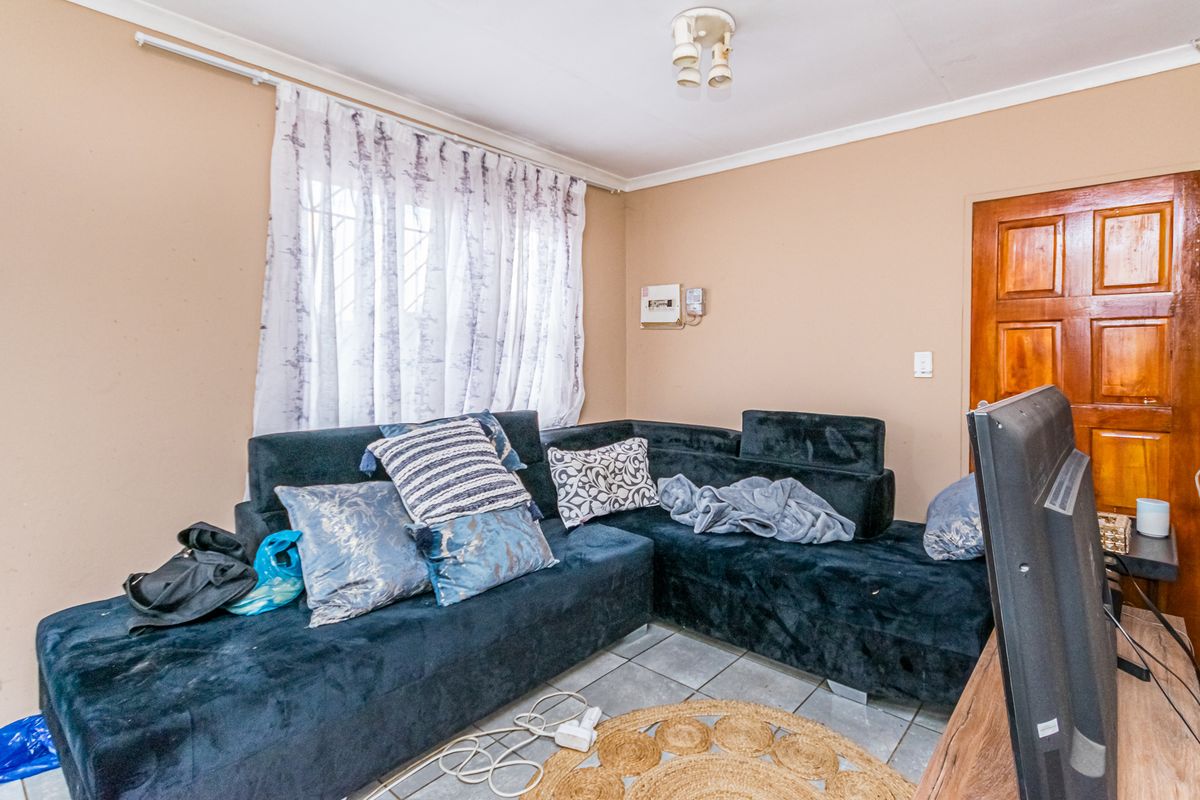 A compact living room featuring tiled flooring, a wooden door, and a window with security bars, providing a functional space for relaxation.
