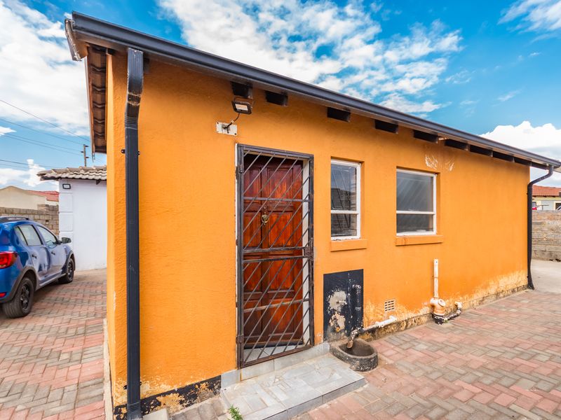 Exterior view of the rear facade featuring orange textured walls, a security gate, and paved ground area.