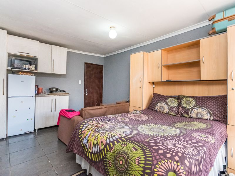 Compact open-plan studio space featuring a kitchenette with built-in cabinetry and a combined living and sleeping area with integrated storage units.