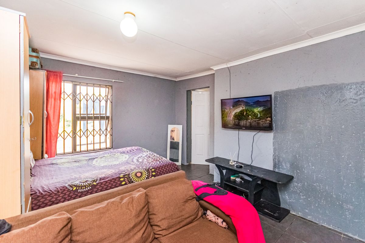 A bedroom featuring tiled flooring, a security gate on the window, and wall-mounted television space with visible wall surface imperfections.