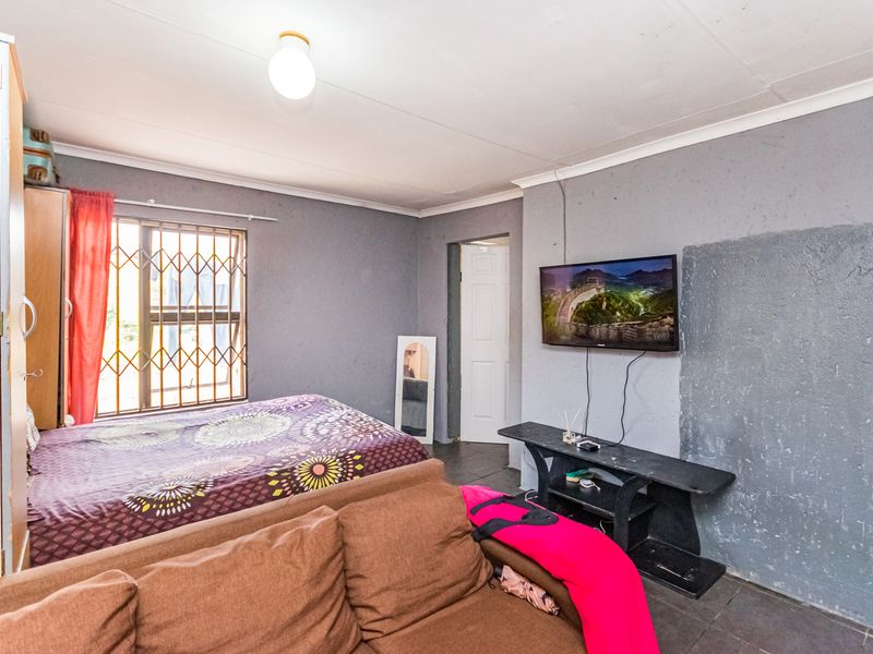 A bedroom featuring tiled flooring, a security gate on the window, and wall-mounted television space with visible wall surface imperfections.