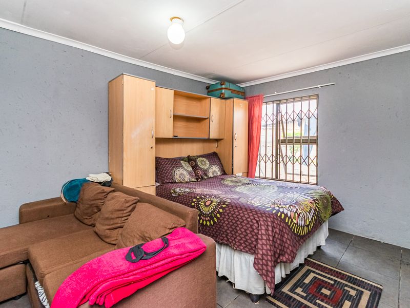 A bedroom featuring tiled flooring, built-in cupboards, and a security gate on the window. The room requires cosmetic updates to the walls.