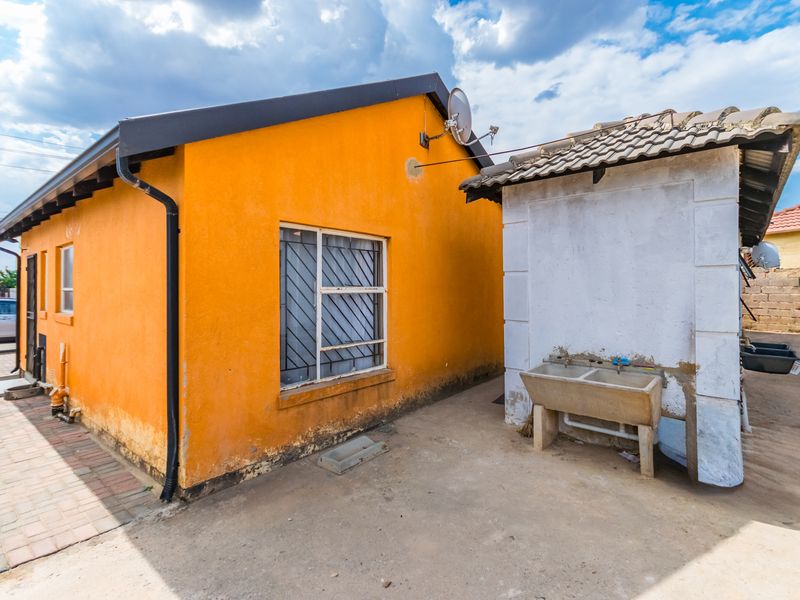 Rear exterior view of the property featuring a concrete wash trough, paved area, and orange painted exterior walls with visible signs of wear.