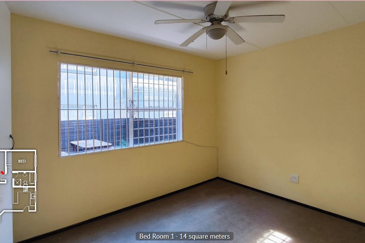 A vacant bedroom featuring a ceiling fan, security bars on the window, and carpeted flooring.