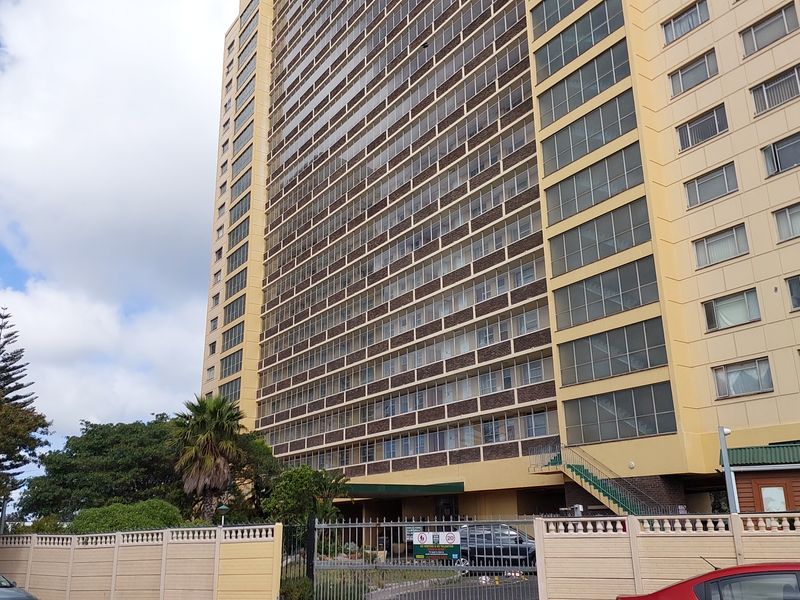 Exterior view of a multi-story apartment building featuring a perimeter wall, security gate, and balcony enclosures.