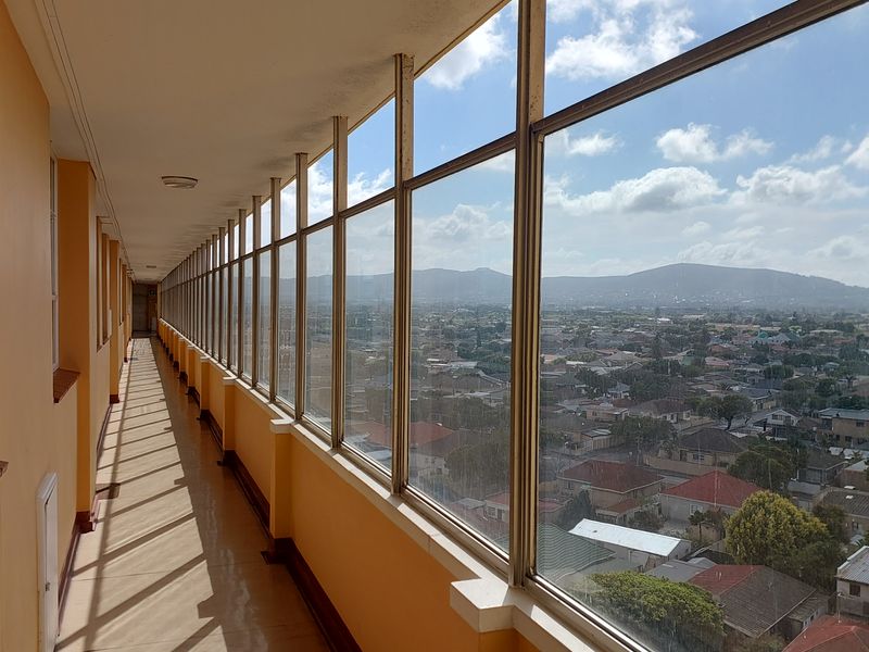 An enclosed balcony or walkway featuring extensive glass paneling with panoramic views of the surrounding residential area and distant mountains.