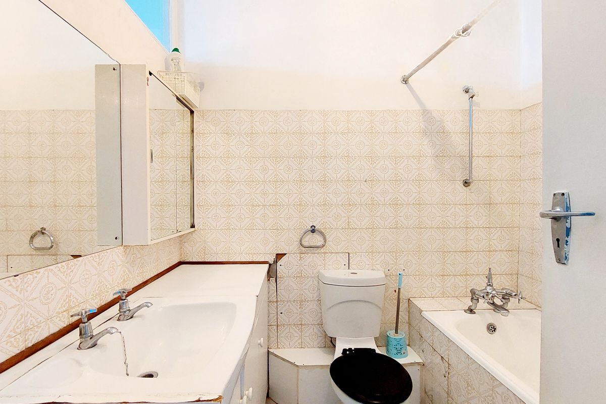 A dated bathroom featuring a built-in vanity, toilet, and bathtub with wall-mounted shower fixtures and classic patterned wall tiling.