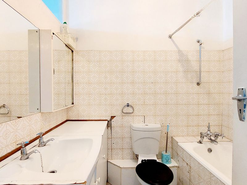 A dated bathroom featuring a built-in vanity, toilet, and bathtub with wall-mounted shower fixtures and classic patterned wall tiling.