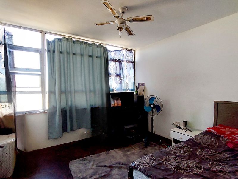 A bedroom featuring a ceiling fan and a large window bank providing natural light, with potential for cosmetic updates to finishes.
