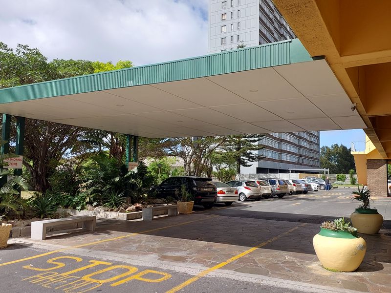 A covered porte-cochere entrance area for the apartment complex, featuring a paved driveway and established garden surroundings.