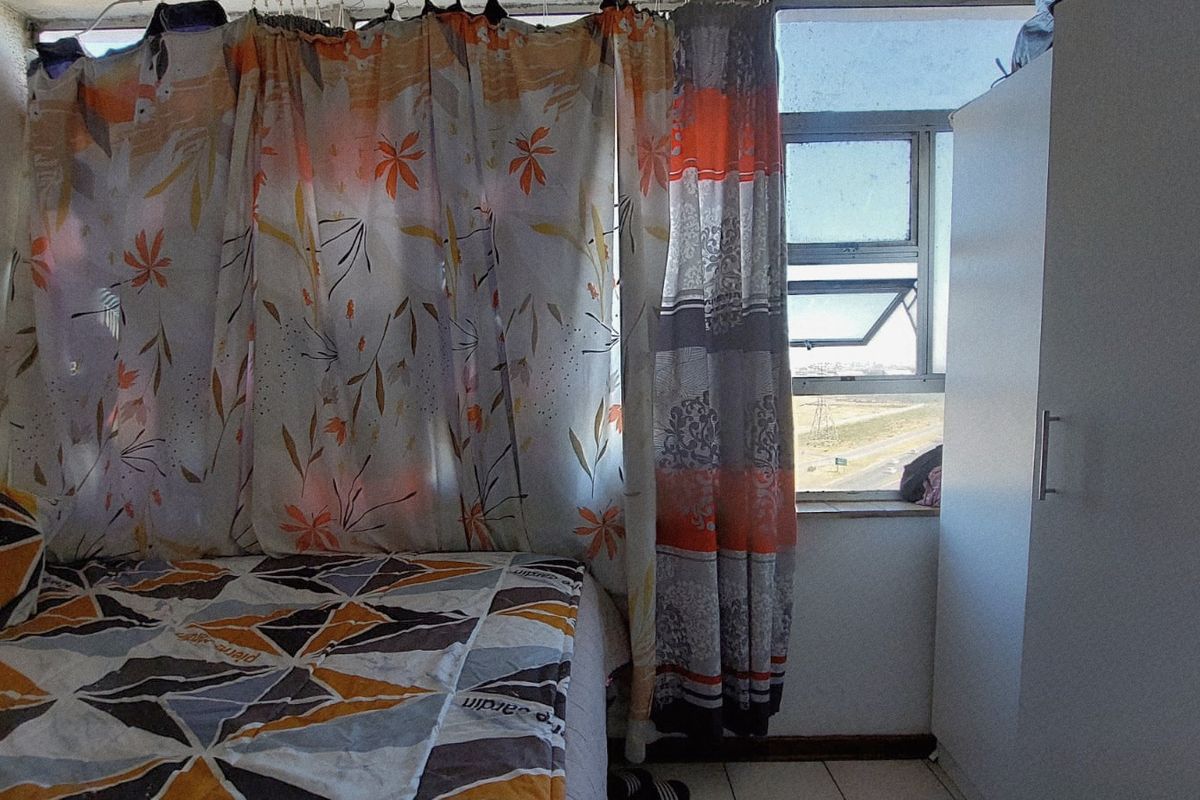A bedroom featuring tiled flooring, a built-in wardrobe, and an aluminium window frame with exterior views.