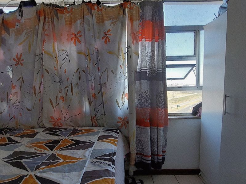 A bedroom featuring tiled flooring, a built-in wardrobe, and an aluminium window frame with exterior views.