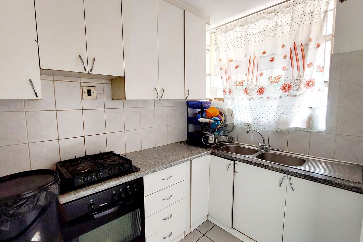 A functional kitchen featuring white built-in cabinetry, laminate countertops, a double stainless steel sink, and a built-in oven with a gas hob.