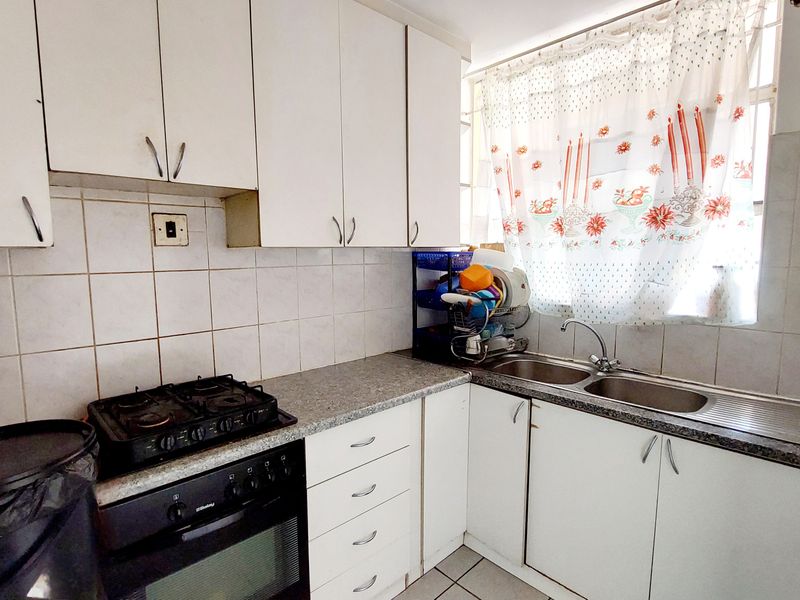 A functional kitchen featuring white built-in cabinetry, laminate countertops, a double stainless steel sink, and a built-in oven with a gas hob.