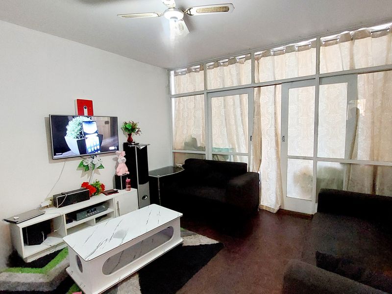 A living room featuring laminate flooring, a ceiling fan, and large glass sliding doors that provide natural light.
