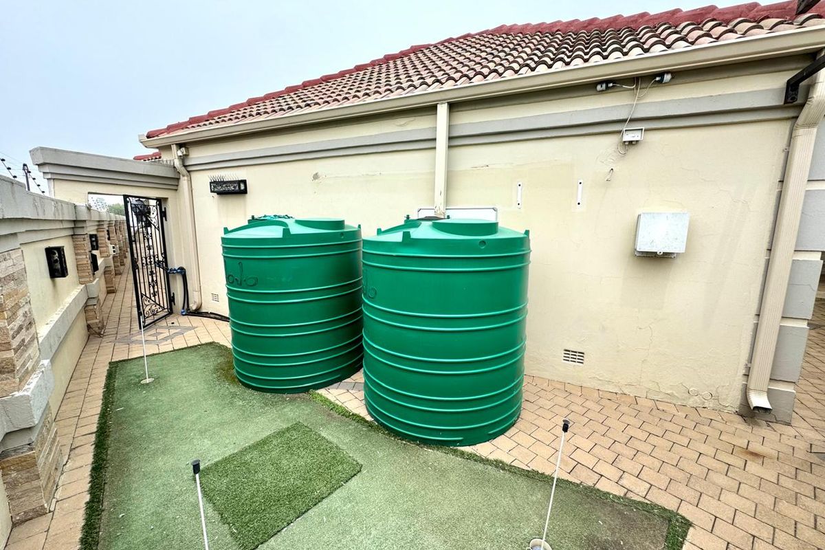 Exterior rear area featuring two large green water storage tanks, paved flooring, and a small artificial putting green surface.