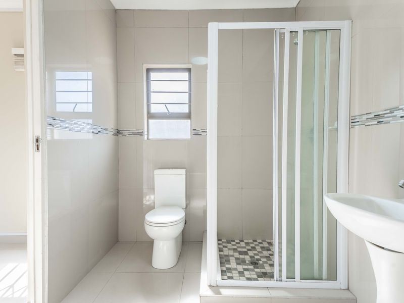 A clean, modern bathroom featuring a shower enclosure, pedestal basin, and toilet with neutral wall and floor tiling.