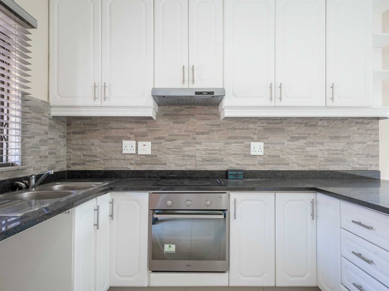 A clean, modern kitchen featuring white cabinetry, granite countertops, a built-in oven with hob, and a stone tile backsplash.