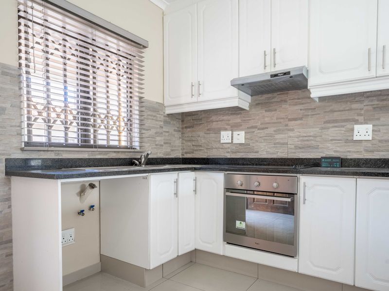A clean, modern kitchen featuring white cabinetry, granite countertops, a stone-cladding backsplash, and integrated stainless steel oven and extractor fan.
