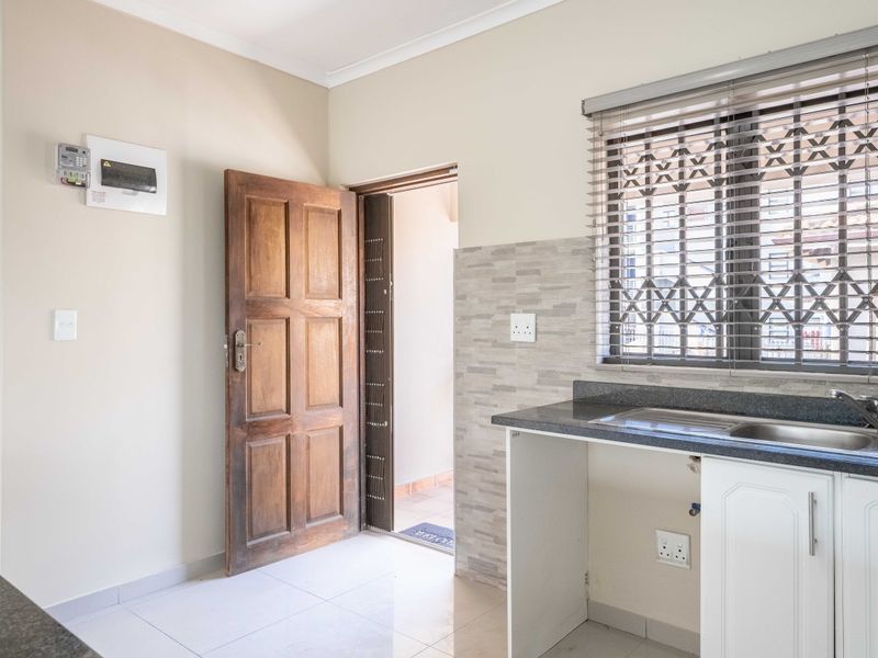 A clean, functional kitchen area featuring a stone countertop, integrated sink, tiled splashback, and direct access to an exterior space.