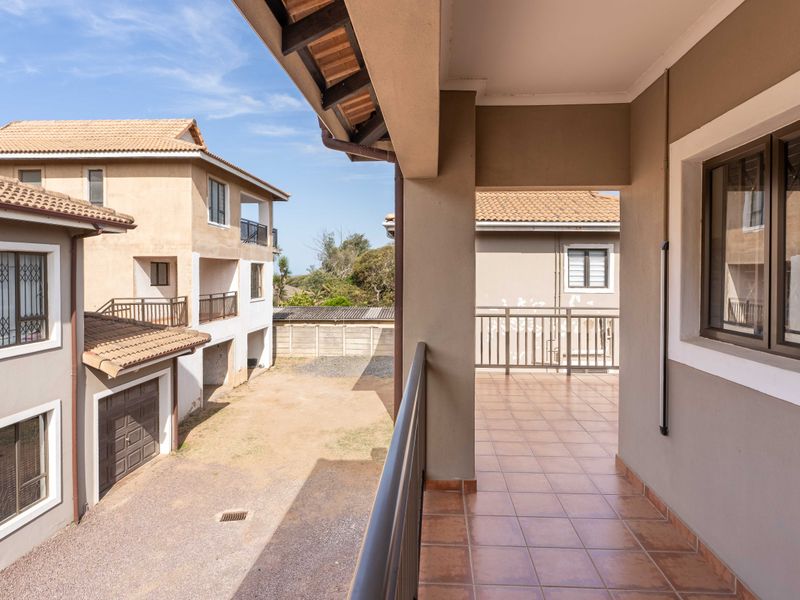 A covered balcony with tiled flooring and metal balustrades, overlooking the complex courtyard and surrounding residential buildings.