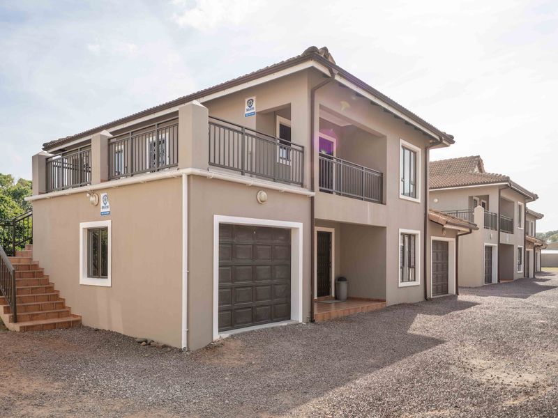 Exterior view of a multi-story residential flat complex featuring tiled roofing, private balconies with metal railings, and integrated garage access.