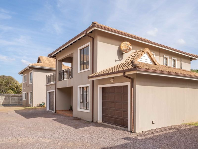 Exterior view of a double-story residential flat featuring a tiled roof, integrated garage, and an upper-level balcony with metal railings.