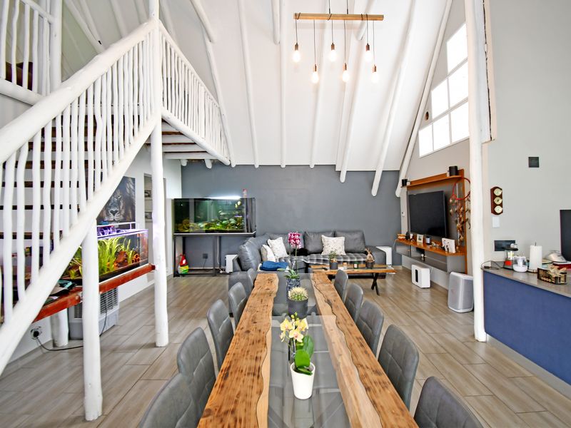 Spacious open-plan living and dining area featuring a high vaulted ceiling with exposed beams, a mezzanine level, and modern tiled flooring.