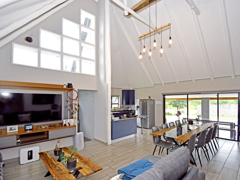 Spacious open-plan living and dining area featuring a dramatic vaulted ceiling with exposed beams, large feature windows, and seamless flow to the outdoor patio.