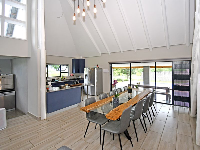 Spacious open-plan kitchen and dining area featuring a vaulted ceiling with exposed rafters, modern cabinetry, and large sliding doors opening to an outdoor patio.