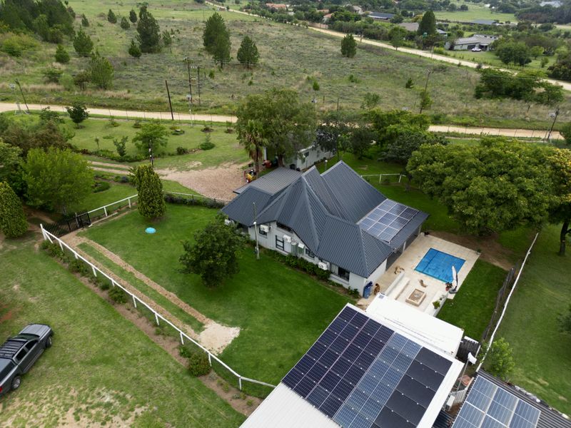 Aerial view of a residential property featuring a metal roof with solar panels, a swimming pool, and a spacious landscaped garden.