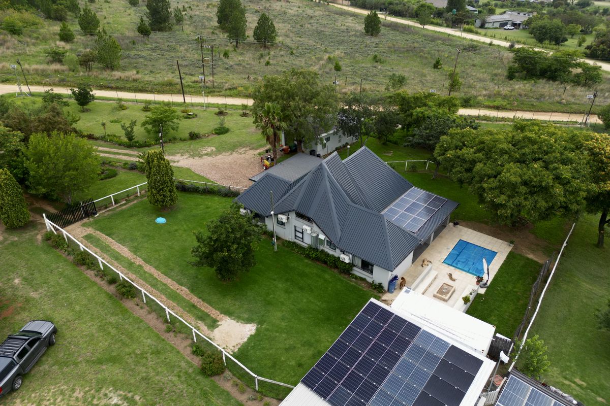 Aerial view of a residential property featuring a metal roof with solar panels, a swimming pool, and a spacious landscaped garden.