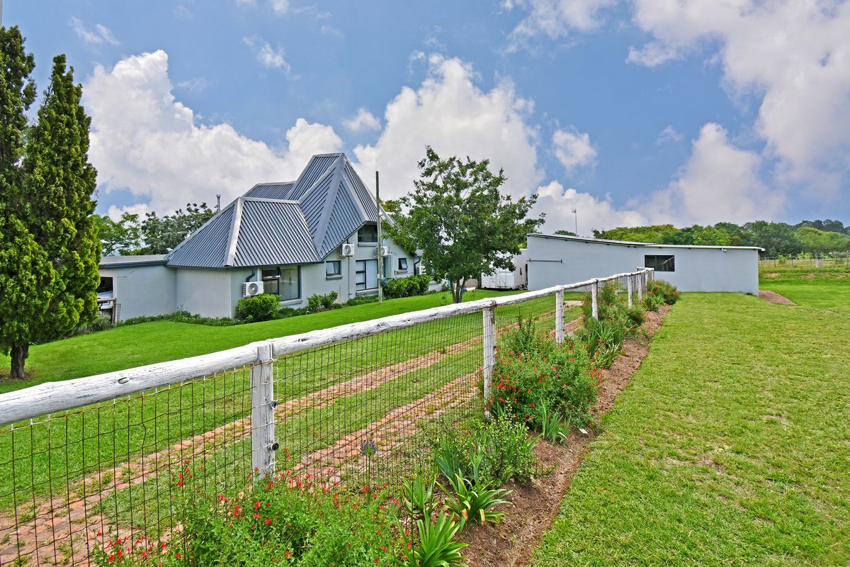 A view of the rear exterior of the house featuring a unique metal roof design, landscaped garden, and wire mesh fencing.