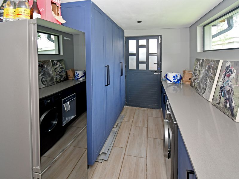 A modern, well-appointed laundry room featuring blue built-in cabinetry, stone countertops, tiled flooring, and direct access to the exterior.